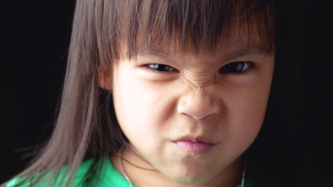 亚洲小女孩的肖像脸，在黑暗的背景上愤怒的表情。