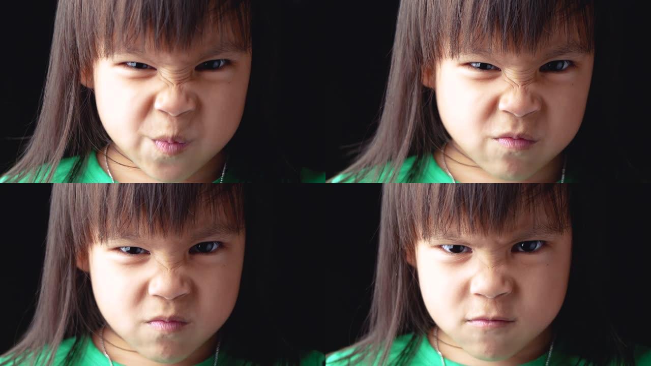 亚洲小女孩的肖像脸，在黑暗的背景上愤怒的表情。