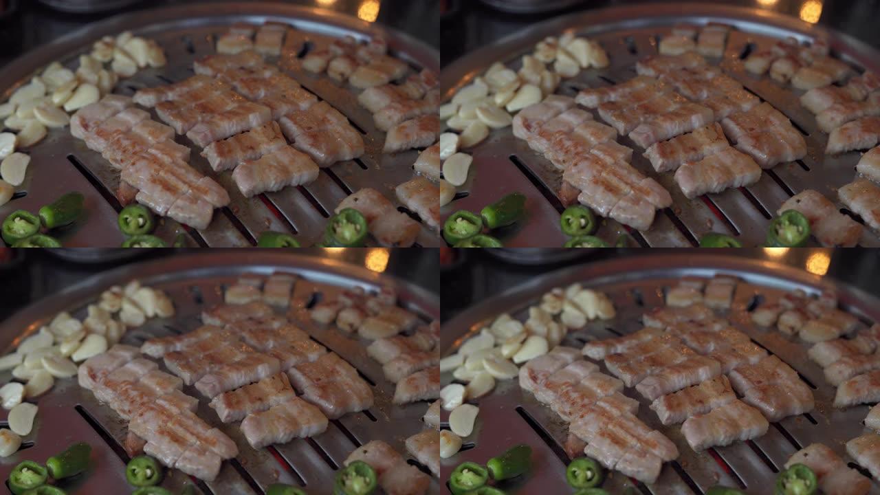 韩国餐厅韩国铁烧烤烤盘上的4K特写烟熏烤猪肚肉和大蒜和青辣椒。传统韩国风格的食物烧烤猪肚牛排在木炭烤
