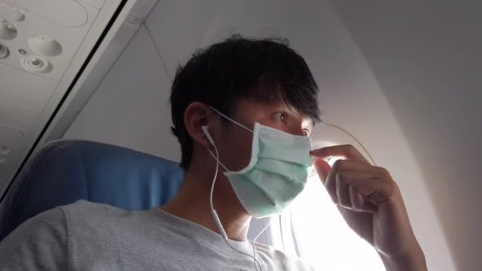 戴着防护面罩的年轻人透过飞机的窗户看起来很担心。