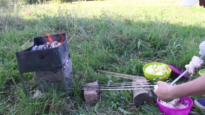 燃烧木材的金属火盆。可见火和烟。一名男子将鸡肉串在串上