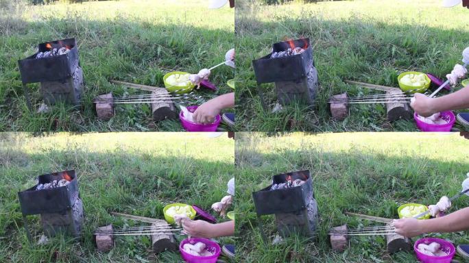 燃烧木材的金属火盆。可见火和烟。一名男子将鸡肉串在串上
