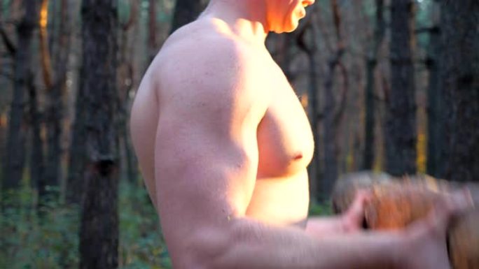 肌肉发达的人，赤裸的躯干举重训练二头肌。强壮的家伙在森林里锻炼。运动员使用原木在户外锻炼。运动的概念