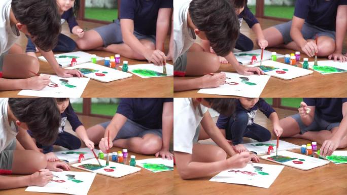一群小孩子坐在地板上，用水彩颜料在纸上画画。大哥和两个兄弟姐妹，兄弟和最小的妹妹周末在客厅里一起休闲