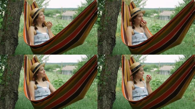 快乐快乐的女人周末在绿色花园的吊床上休息。年轻女子躺在吊床上，在乡下享受暑假。黑发女性吃苹果，在吊床