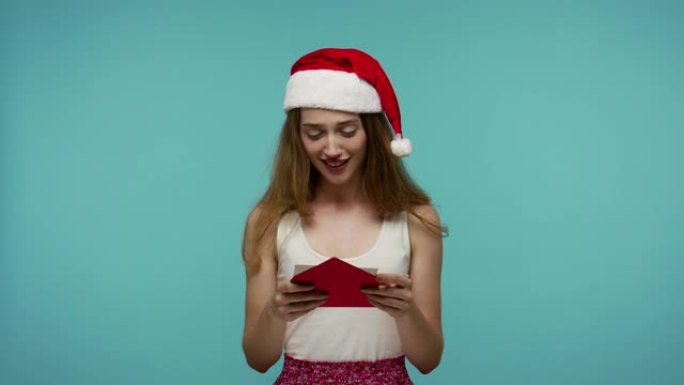 可爱的可爱的圣诞精灵女孩戴着圣诞老人帽子阅读信信封，上面有礼物清单，微笑着甜蜜