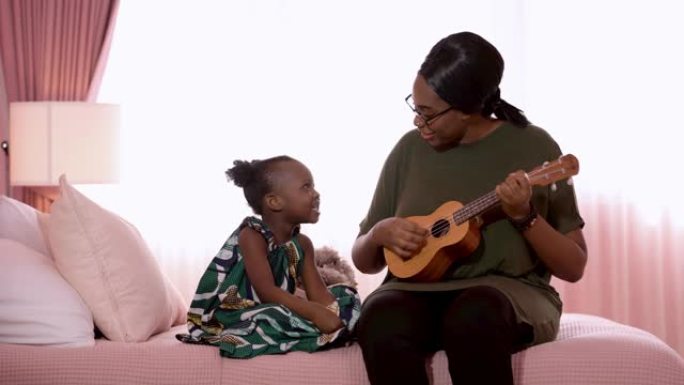 快乐的家庭非洲母亲和孩子一起唱歌和弹吉他，同时坐在卧室的床上。