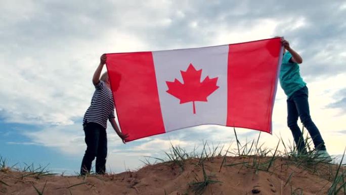 4k。夏天，金发男孩和女孩在蓝天上户外挥舞加拿大国旗 -- 加拿大日，国家，爱国主义，独立日7月1日