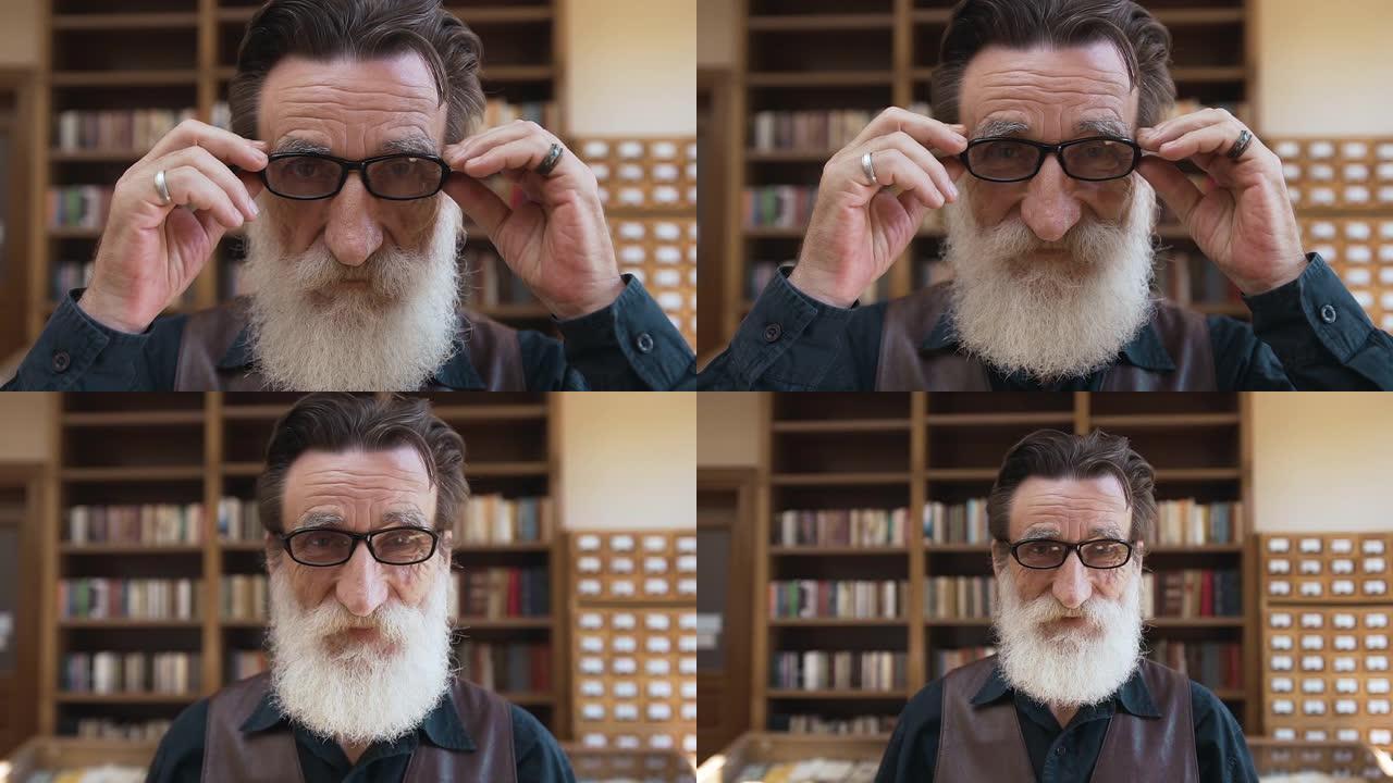英俊的经验丰富的胡子男人，满脸皱纹，戴上眼镜，在图书馆里真诚地微笑着对着镜头摆姿势