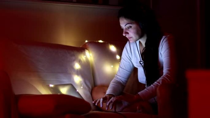 女人晚上使用笔记本电脑，将耳机放在浏览互联网上