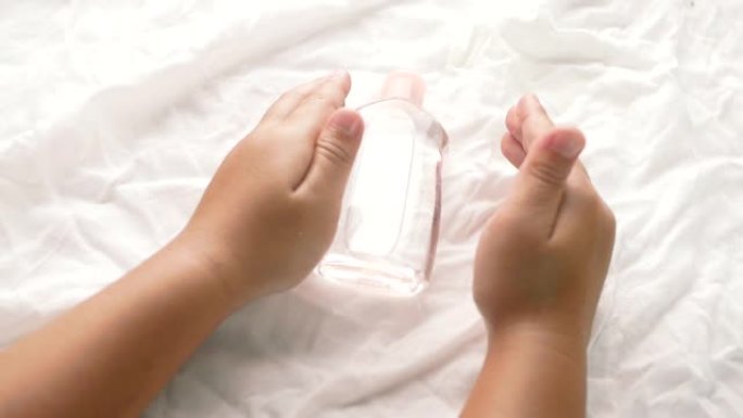 小手在白色织物背景上拿着透明塑料瓶油的特写镜头。关心柔软的身体婴儿皮肤。
