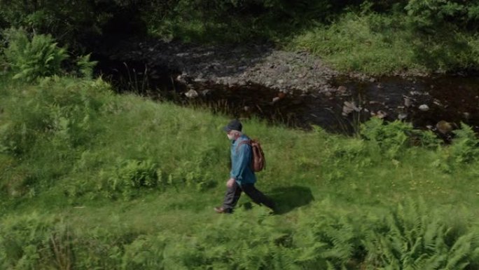 活跃的高级男子在苏格兰西南部偏远农村的一条缓慢流动的小河旁行走