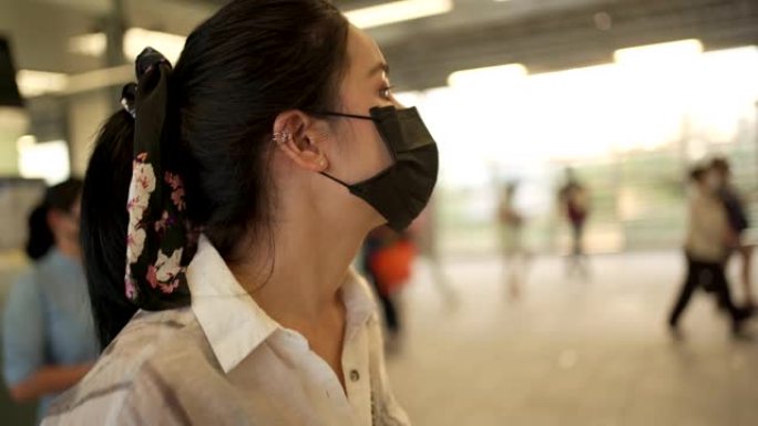 年轻的亚洲妇女戴着黑色防护口罩站在地铁应变站内。新型冠状病毒肺炎女士等待朋友，公共交通医疗保健高峰时