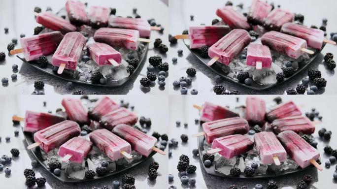 自制新鲜冷冻蓝莓和黑莓冰棍放在黑色盘子上，冰放在石头上