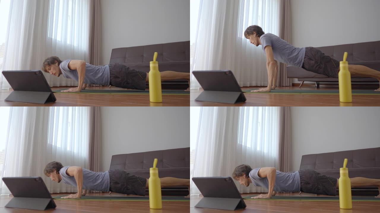 一个年轻人在家按照他在平板电脑上观看的视频中的指示进行体育锻炼。社会距离概念。互联网培训师概念