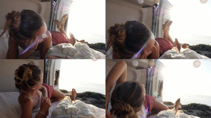 女性在度假期间在面包车里放松。乘坐露营车旅行的年轻女子从她家欣赏海岸景色。另类生活