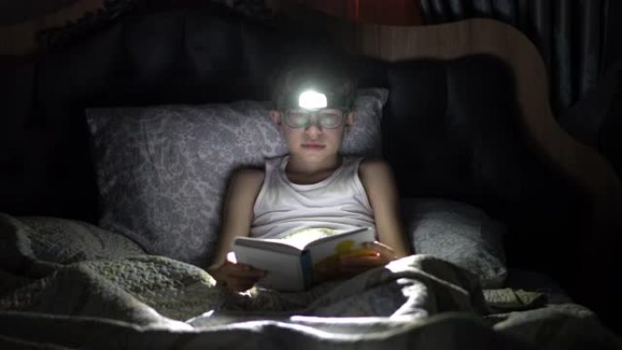 小男孩在床上用手电筒看书