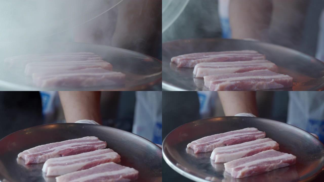 4k特写镜头熏制生五花肉，准备在餐厅的韩国铁烧烤烤盘上烧烤。传统韩国风格的食物烧烤猪肚牛排在木炭烤架