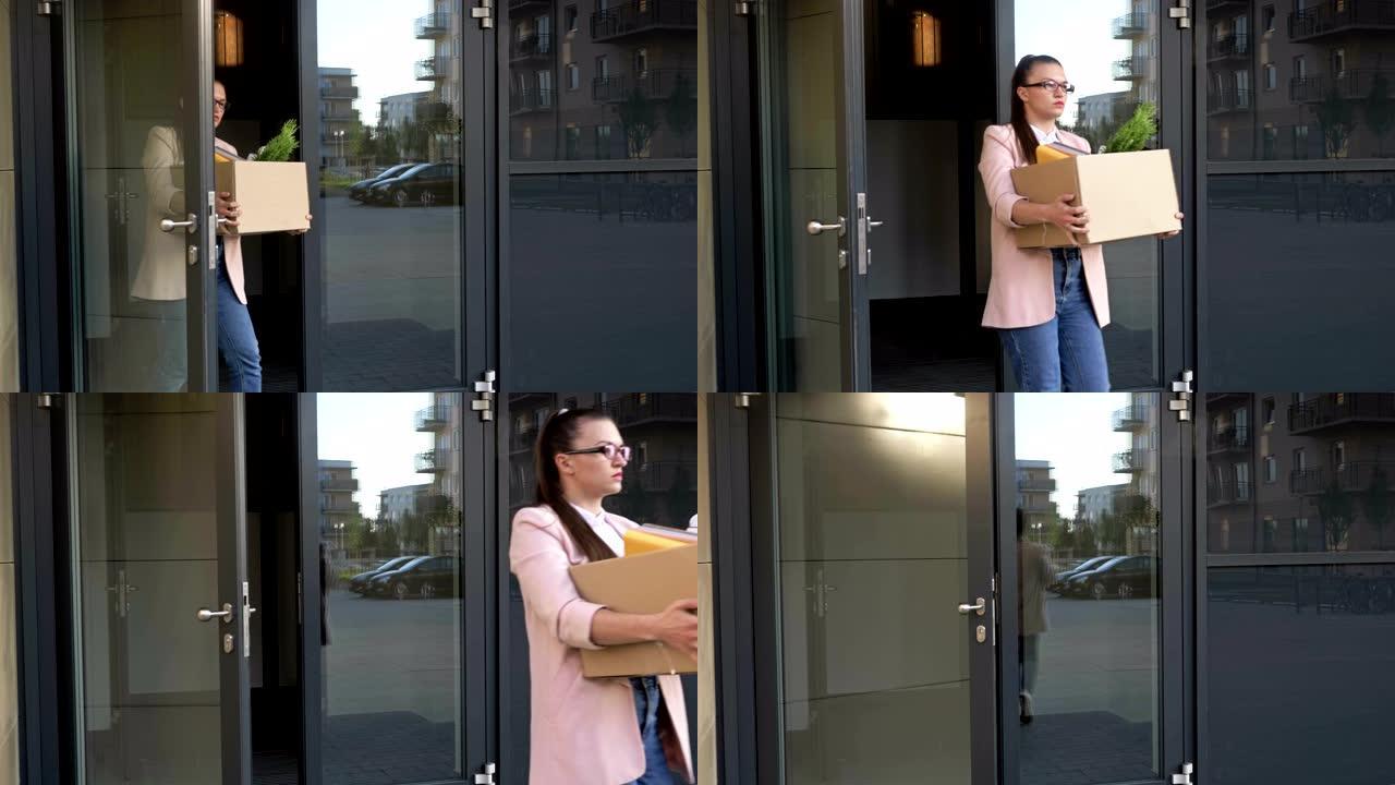 刚刚失业的悲伤年轻女子走出办公室大门。她手里是一个装有个人物品的盒子。经济危机