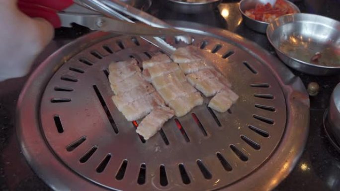 在韩国餐厅，厨师手用食物剪剪烟熏烤架猪肚肉在韩国铁烧烤烤盘上拍摄4k特写镜头。传统的韩式食品烧烤猪肚
