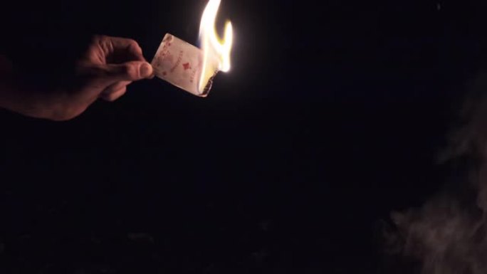 手在大自然篝火附近的黑色背景上拿着燃烧卡。慢动作