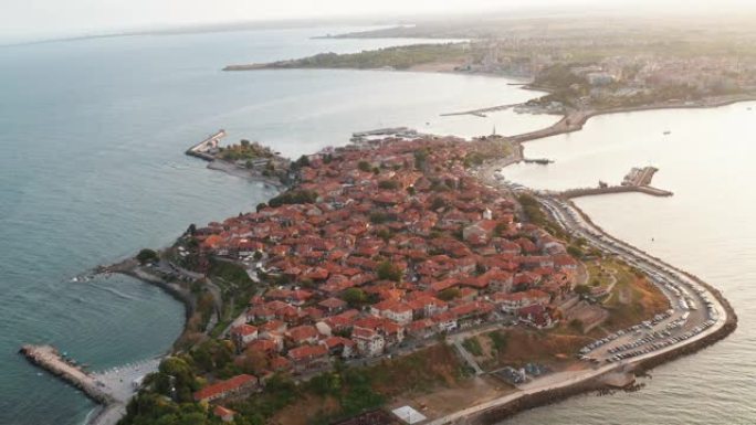 在夏天的海上日落日，从无人机飞行的鸟瞰图看到很多红色瓷砖房屋的屋顶，向前转向保加利亚半岛的老度假小镇