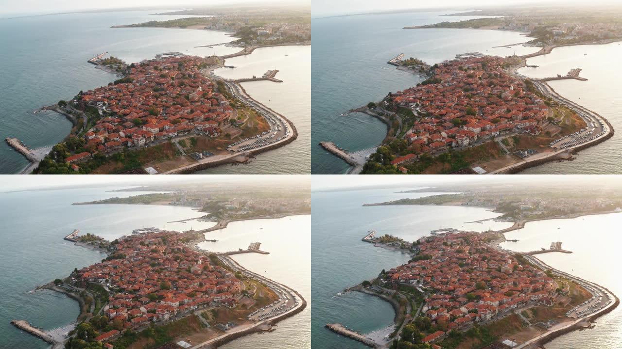 在夏天的海上日落日，从无人机飞行的鸟瞰图看到很多红色瓷砖房屋的屋顶，向前转向保加利亚半岛的老度假小镇