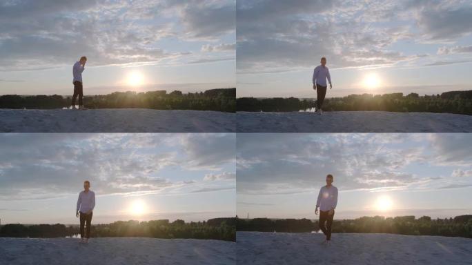在一个美丽的夏日夜晚，日落时分，英俊的沉思的家伙赤脚走在沙滩上。情绪。慢动作镜头