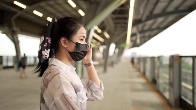 亚洲女性通勤者戴黑色面具站在天空火车平台上，新型冠状病毒肺炎大流行，地铁站内孤独无望的女人新常态，调