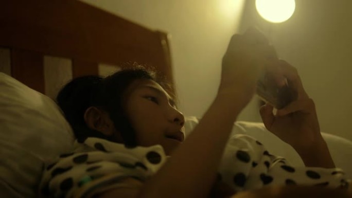 亚洲女孩使用智能手机在家里的床上看电影或玩网络游戏，有夜灯。