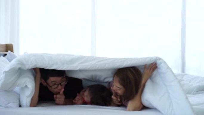 亚洲自闭症障碍小女孩和父母在白色床上玩耍，躲在房子里的白色毯子下