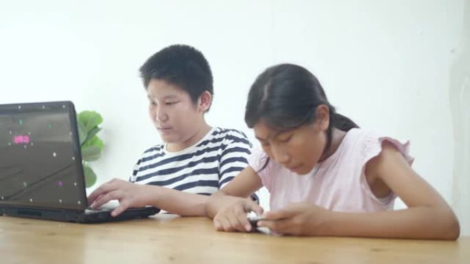 快乐的亚洲兄弟和她的妹妹玩游戏与笔记本电脑和智能手机在线竞争在家里，生活方式的概念。