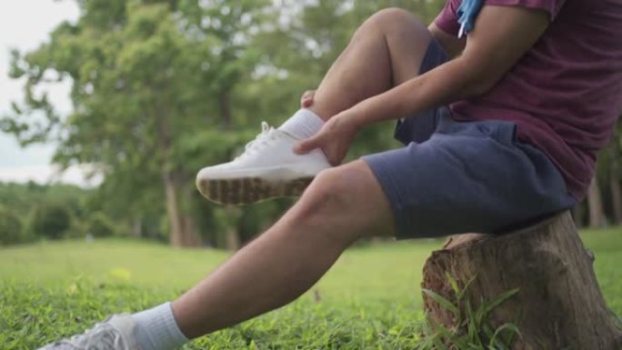 亚洲男子在公园内运动时扭伤了脚踝坐在树干上，背景是草坪，脚踝疼痛，关节韧带问题，痛苦的表情，事故风险