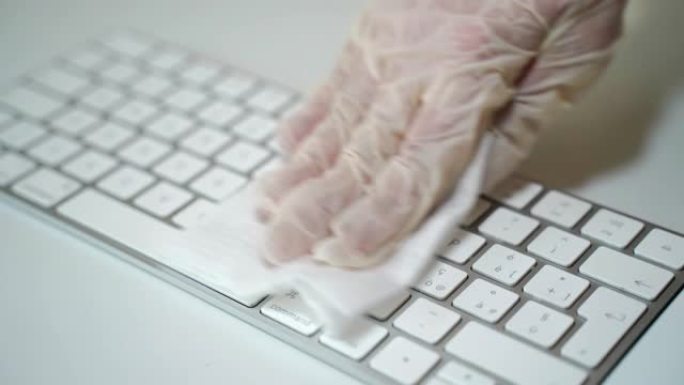戴着白色防护手套的人使用湿抗菌擦拭并清除键盘表面的脏污，微生物和细菌。新型冠状病毒肺炎大流行期间的卫