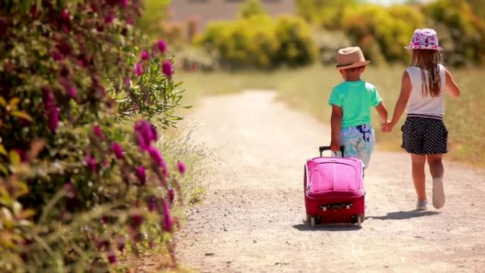 戴着帽子的可爱孩子带着一个粉红色的手提箱一起走在马路上