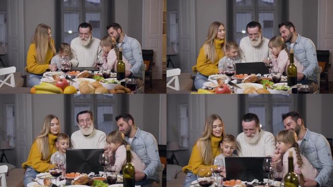 尊敬的祖父在餐桌上打开计算机，并与家人一起观看照片