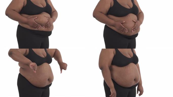 无法辨认的黑人肥胖妇女穿着内衣的身体的特写镜头，从腹部摇晃她的脂肪，并在白色背景上显示拇指向下孤立