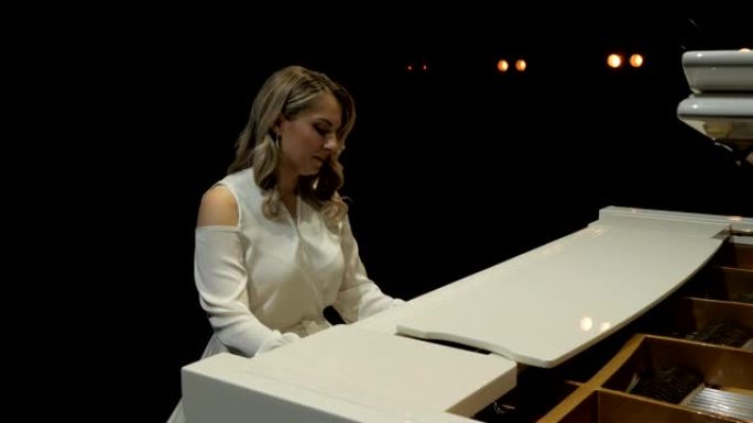舞台上的白色三角钢琴。微笑的女钢琴家在音乐厅的舞台上演奏大钢琴。