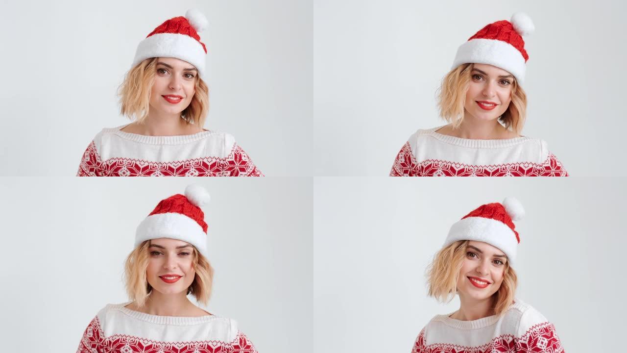 圣诞小红帽装扮的金发女郎面带微笑，随着音乐起舞，在白色背景上带着节日的气氛看着镜头。圣诞老人的帮手。