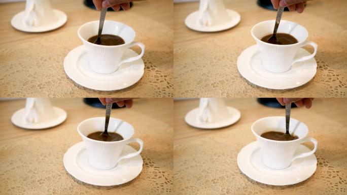 人用勺子在木桌背景上的白色杯子里用手搅拌咖啡的特写镜头。