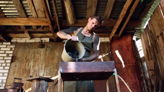 一个戴着面纱的男铁匠将煤从水桶倒入锻造炉中。