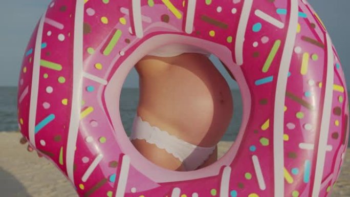 穿着粉红色充气甜甜圈的孕妇的肚子。特写。