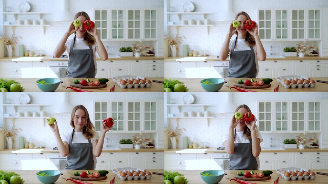 美女在家庭厨房玩两个辣椒。情绪化的女人用绿色和红色的辣椒粉做脸