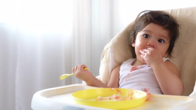 可爱的蹒跚学步的女婴喜欢在家里的婴儿椅上吃蛋糕或甜食。可爱的小女孩或女儿吃完了蛋糕，婴儿想要更多的蛋