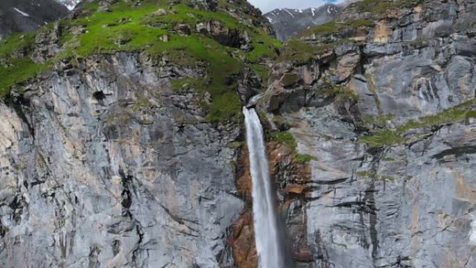 空中慢动作: 无人机飞越风景秀丽的高瀑布，从意大利阿尔卑斯山茂密的高大岩石悬崖上掉落的山流