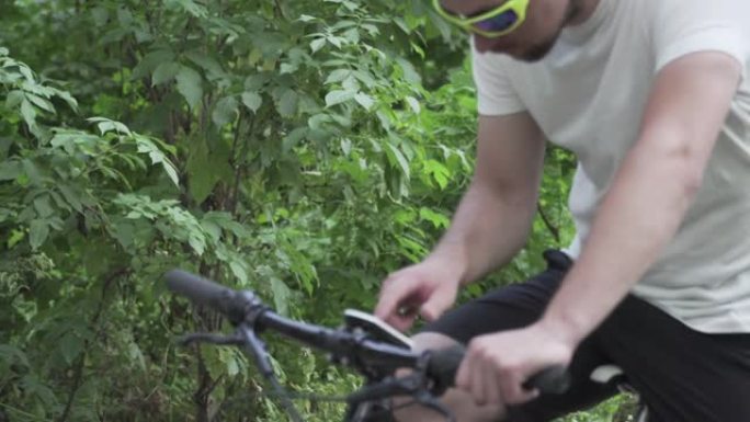 穿着运动服的男性在山地自行车上使用小工具在自行车电脑上导航。男子运动员在森林里锻炼，手里拿着全球定位