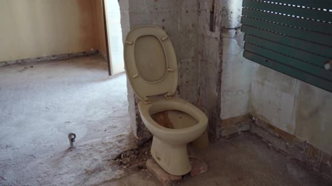 废弃房屋中的老生锈肮脏的黄色厕所，陶瓷堵塞的厕所靠在剥皮的墙上。室内照片被摧毁的公寓，浴室被毁，厕所