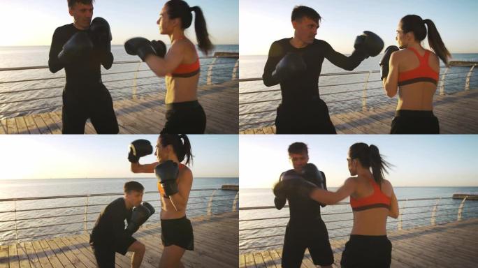 穿着运动服的年轻女性正在和她的职业教练一起拳击。他们躲避拳头，在海滨长廊上练习锻炼。慢动作