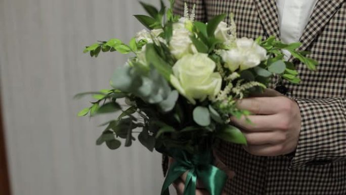 新郎手里拿着婚礼花束在家里。白衬衫，夹克。特写镜头。慢动作