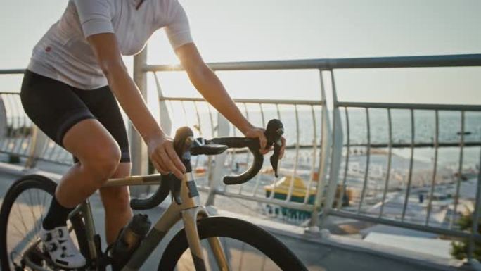 穿着运动服的不知名女性正沿着海边附近的布里奇 (bridge) 下坡骑现代自行车。夏季晴天，慢动作